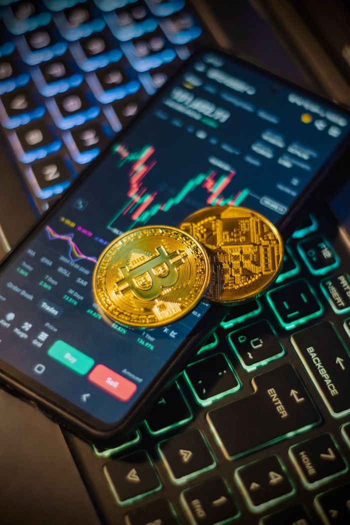 services-01 Cryptocurrency trading interface on a mobile with Bitcoin coins on a laptop keyboard.